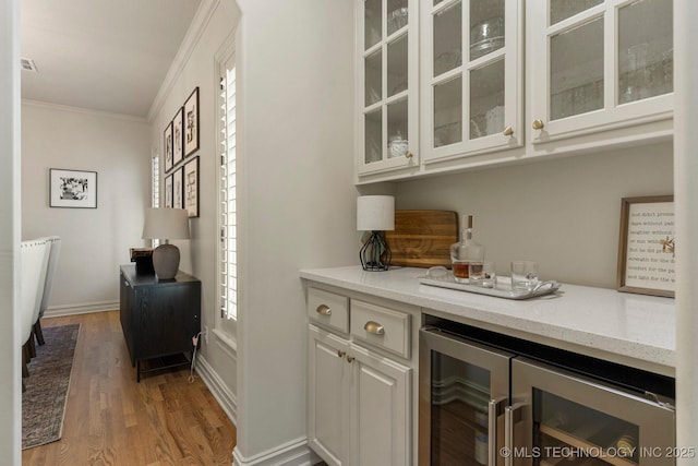 bar with hardwood / wood-style floors, white cabinets, wine cooler, light stone countertops, and ornamental molding