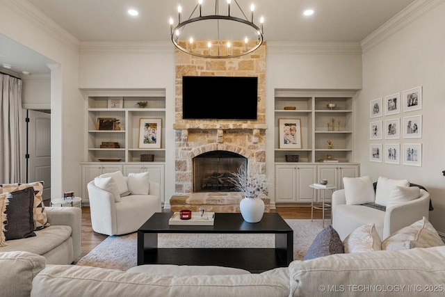 living room with built in shelves, hardwood / wood-style flooring, a stone fireplace, and a notable chandelier