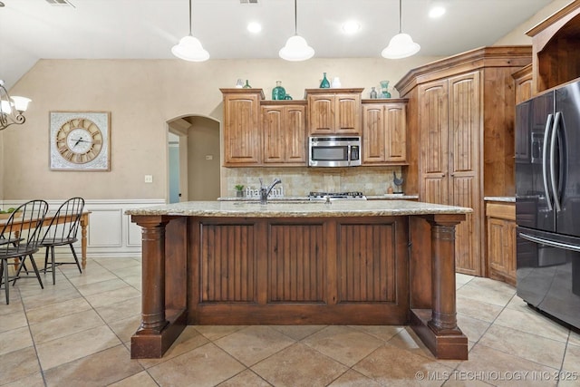 kitchen featuring a center island with sink, decorative light fixtures, refrigerator, and decorative backsplash