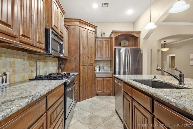 kitchen with sink, stainless steel appliances, light stone counters, backsplash, and decorative light fixtures