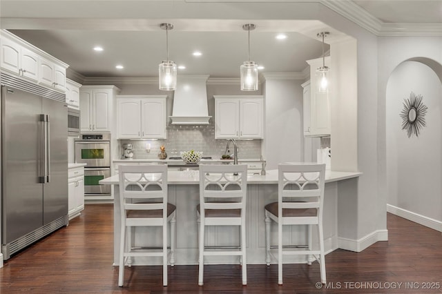 kitchen featuring appliances with stainless steel finishes, white cabinetry, a kitchen breakfast bar, and custom exhaust hood