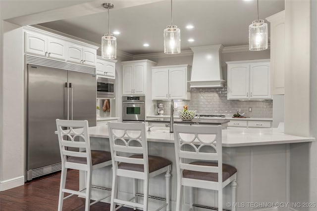 kitchen featuring custom range hood, built in appliances, and white cabinetry