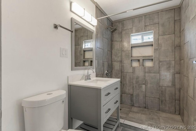 bathroom with a tile shower, vanity, and toilet