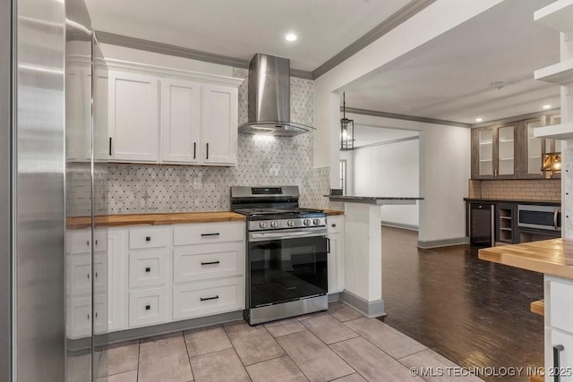 kitchen with wall chimney range hood, wood counters, appliances with stainless steel finishes, white cabinets, and ornamental molding