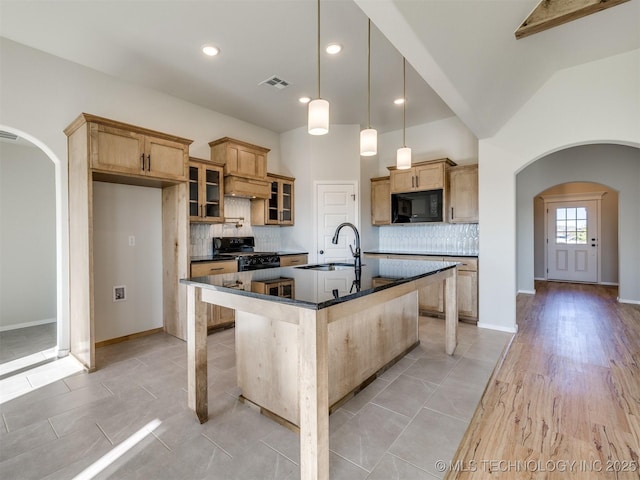 kitchen featuring backsplash, vaulted ceiling, sink, black appliances, and a center island with sink