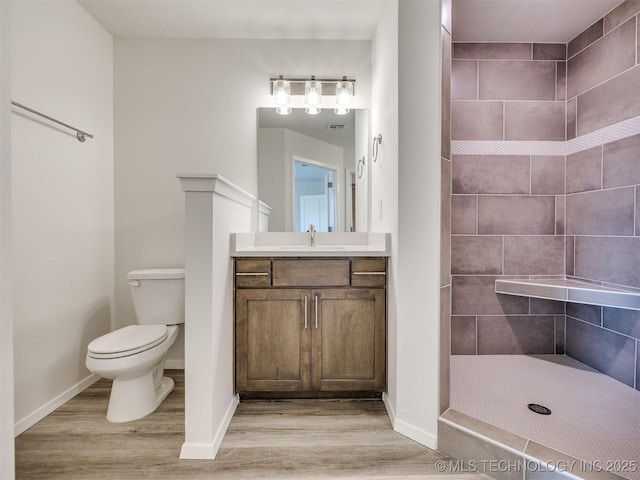 full bath with a tile shower, wood finished floors, toilet, and vanity