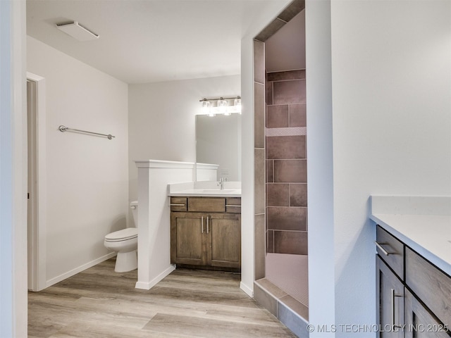 full bathroom featuring wood finished floors, toilet, vanity, baseboards, and tiled shower