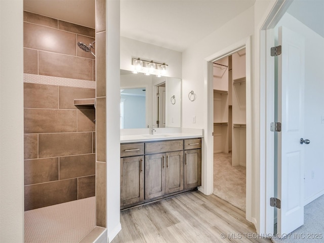 full bath featuring a walk in closet, walk in shower, vanity, and wood finished floors