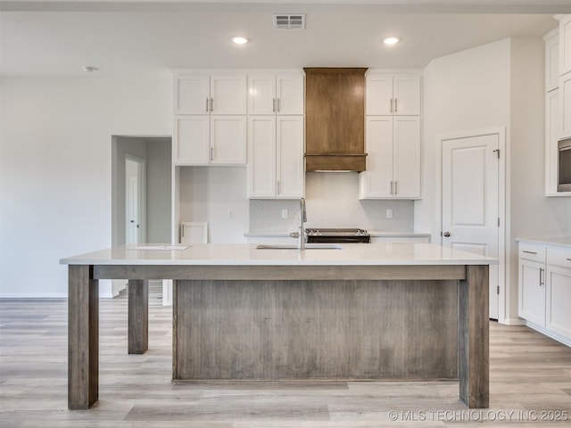kitchen featuring white cabinetry, an island with sink, and visible vents