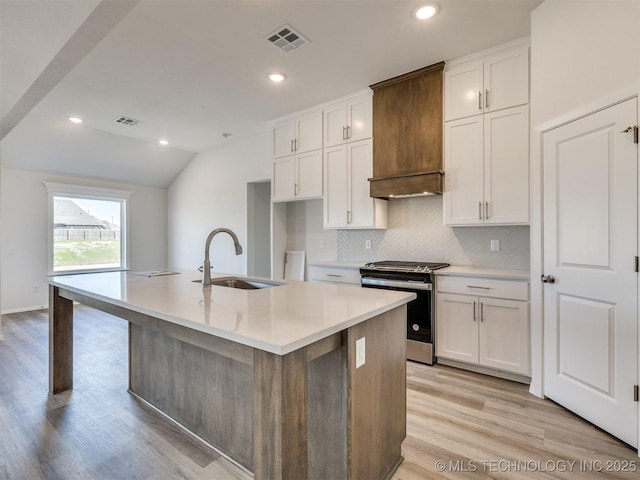 kitchen with stainless steel range with gas cooktop, a sink, decorative backsplash, light wood-style flooring, and visible vents