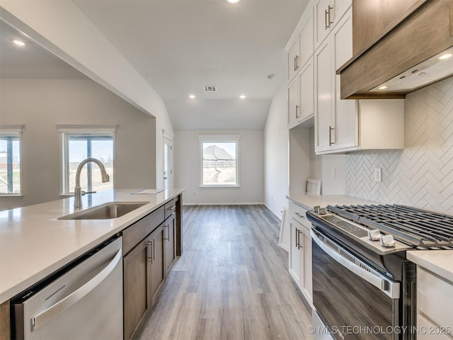 kitchen with a sink, backsplash, light wood-style floors, light countertops, and appliances with stainless steel finishes