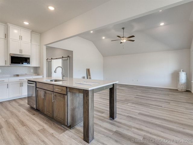 kitchen with lofted ceiling, light wood finished floors, stainless steel appliances, a ceiling fan, and a sink