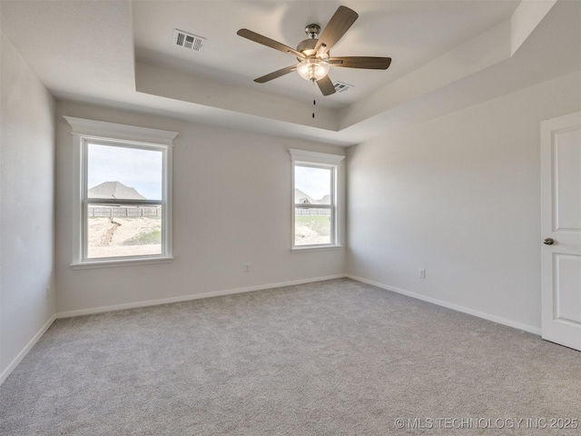 spare room featuring a raised ceiling, visible vents, ceiling fan, and a healthy amount of sunlight