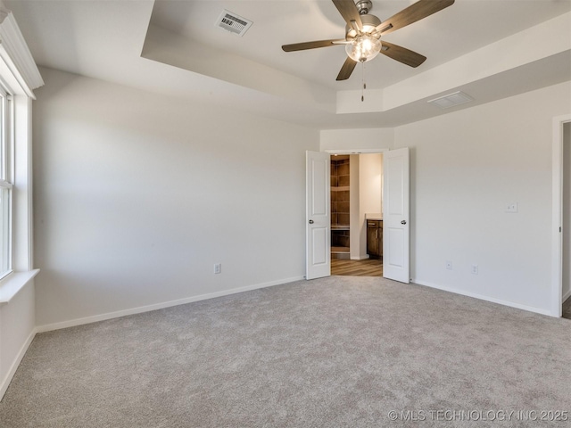 unfurnished bedroom with baseboards, visible vents, carpet floors, and a tray ceiling