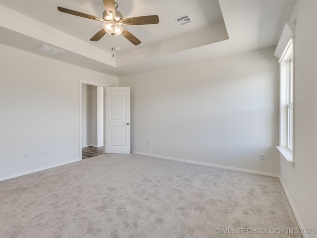 carpeted empty room featuring a tray ceiling, visible vents, baseboards, and ceiling fan