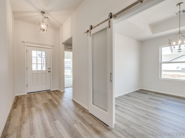 foyer featuring light wood finished floors, a barn door, baseboards, visible vents, and a notable chandelier