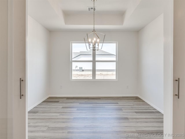 empty room with a raised ceiling, light wood-style floors, visible vents, and a notable chandelier