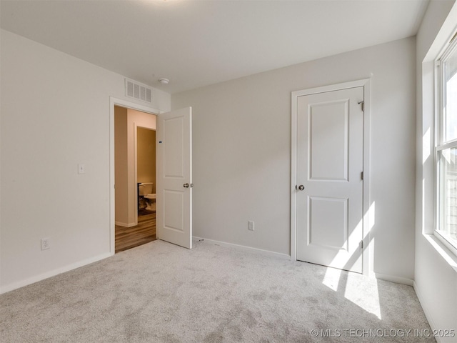unfurnished bedroom with carpet floors, multiple windows, visible vents, and baseboards