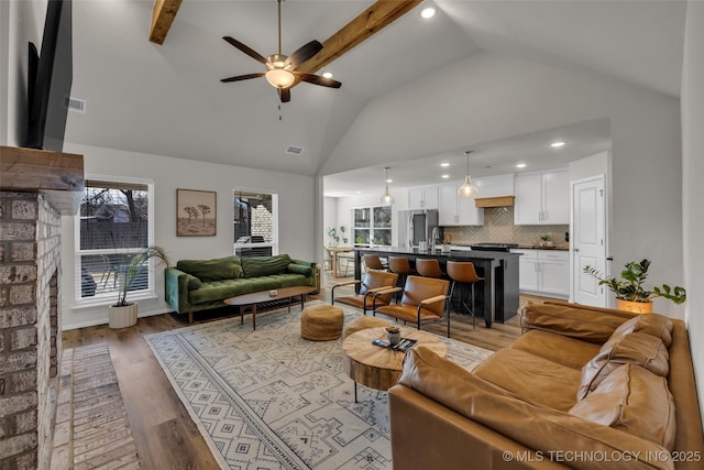 living room with lofted ceiling with beams, sink, a brick fireplace, light hardwood / wood-style flooring, and ceiling fan