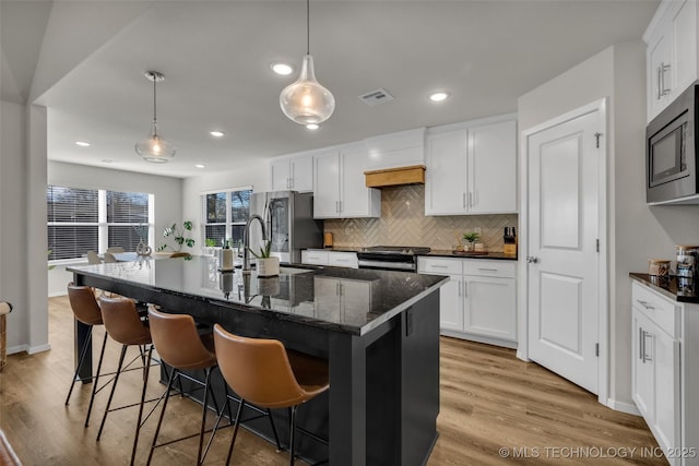 kitchen with decorative light fixtures, a kitchen bar, an island with sink, and stainless steel appliances