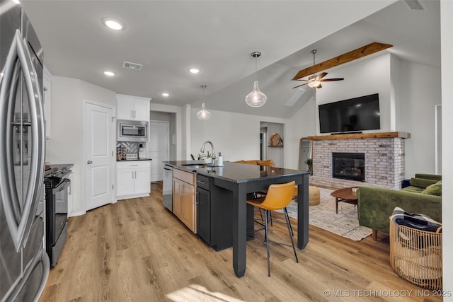 kitchen featuring white cabinetry, stainless steel appliances, a brick fireplace, a kitchen breakfast bar, and a center island with sink