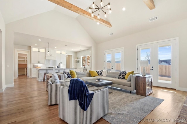 living room with high vaulted ceiling, an inviting chandelier, french doors, light hardwood / wood-style floors, and beam ceiling