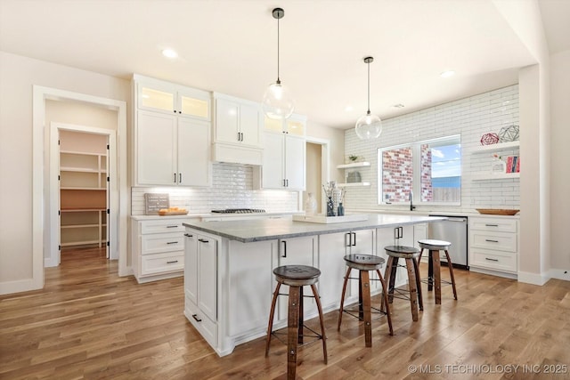 kitchen featuring dishwasher, decorative backsplash, light wood-type flooring, a kitchen bar, and white cabinetry