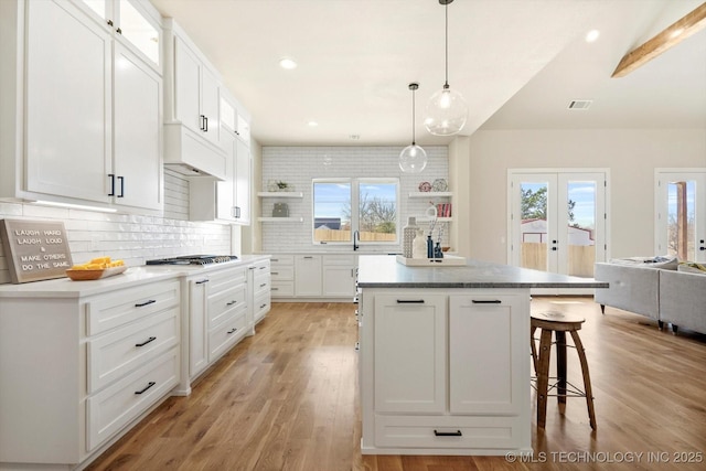 kitchen featuring pendant lighting, a center island, french doors, white cabinets, and tasteful backsplash