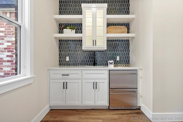 bar with decorative backsplash, light wood-type flooring, white cabinetry, and sink