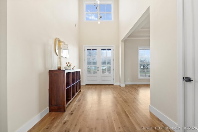 foyer featuring a chandelier, light wood-type flooring, ornamental molding, and french doors