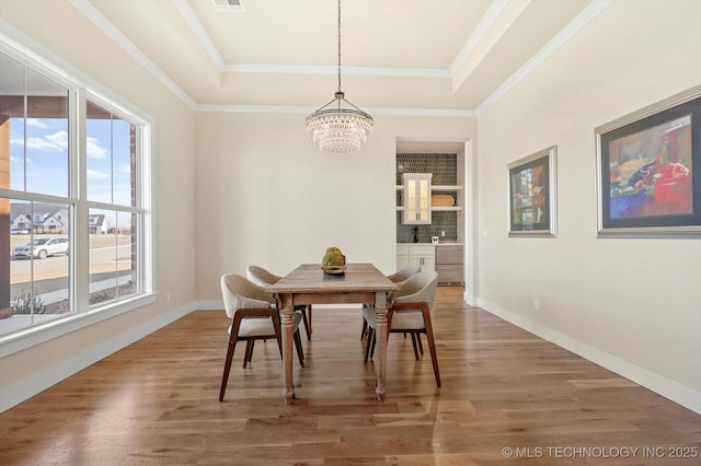 dining area with a raised ceiling, wood-type flooring, ornamental molding, and a chandelier