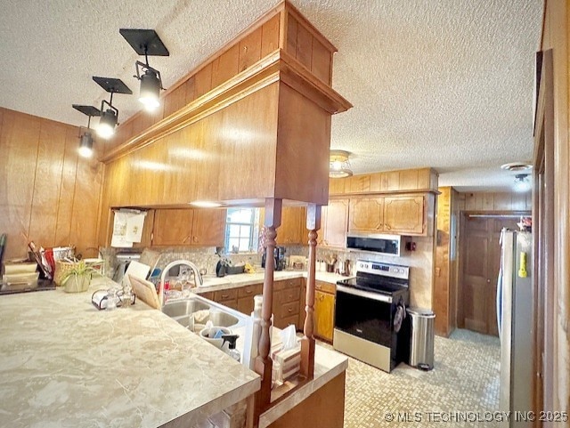 kitchen featuring stainless steel appliances, wood walls, a peninsula, and light countertops