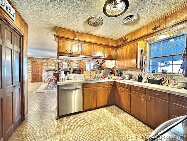 kitchen featuring brown cabinets, light countertops, a peninsula, and stainless steel dishwasher