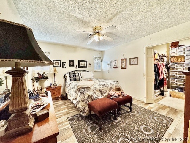 bedroom featuring a textured ceiling, a spacious closet, a ceiling fan, and light wood-style floors