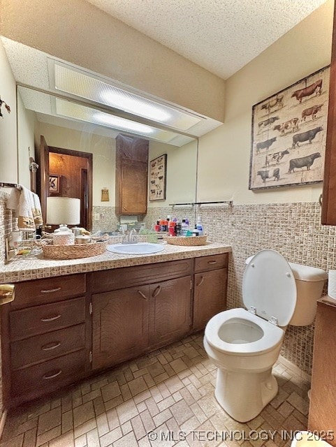 bathroom with a textured ceiling, toilet, vanity, tile walls, and wainscoting