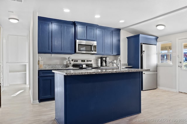 kitchen featuring appliances with stainless steel finishes, light wood-type flooring, a center island with sink, and blue cabinets