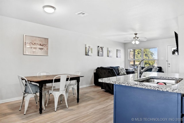 kitchen featuring sink, ceiling fan, blue cabinetry, light hardwood / wood-style floors, and light stone counters