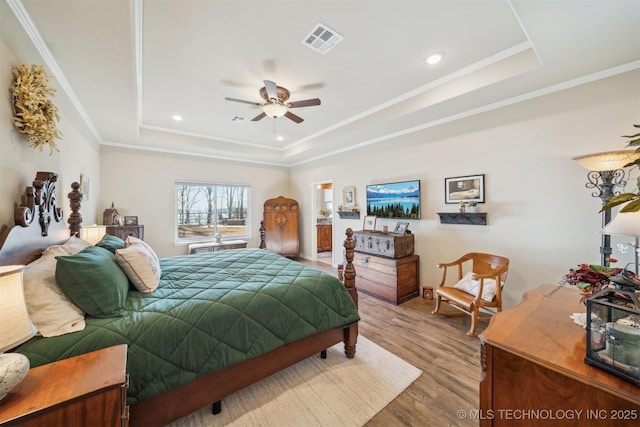 bedroom featuring visible vents, a raised ceiling, wood finished floors, and ornamental molding