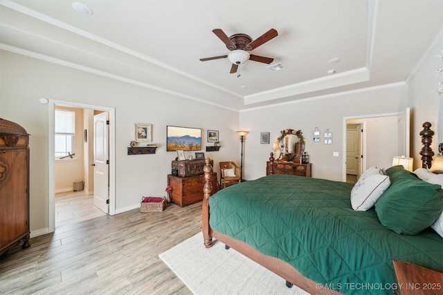 bedroom featuring light wood-type flooring, ensuite bath, a tray ceiling, ceiling fan, and crown molding