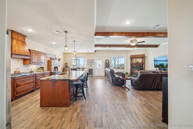 kitchen with pendant lighting, a breakfast bar, a large island with sink, light hardwood / wood-style flooring, and tasteful backsplash