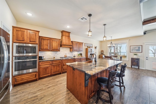 kitchen featuring custom exhaust hood, a kitchen island with sink, a breakfast bar area, dark stone countertops, and stainless steel appliances