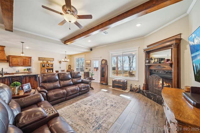 living room featuring crown molding, a fireplace, wood finished floors, beamed ceiling, and ceiling fan with notable chandelier