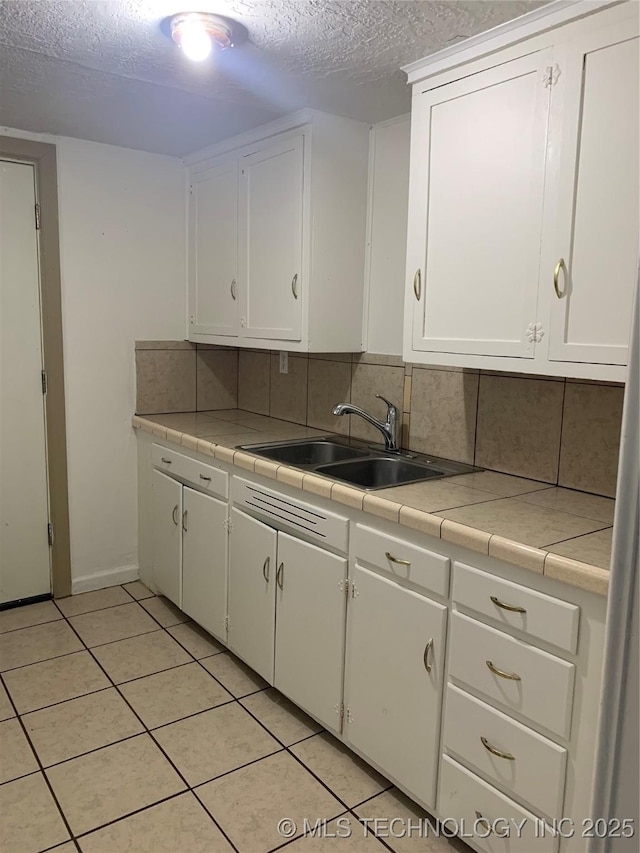 kitchen with white cabinets, backsplash, tile counters, and sink