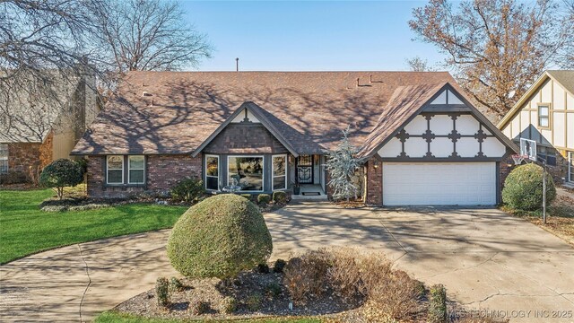 tudor-style house featuring a front lawn, a garage, brick siding, and driveway