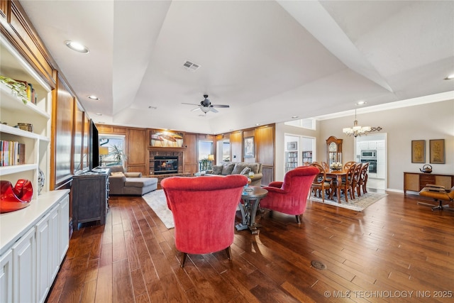 living room with a glass covered fireplace, ceiling fan with notable chandelier, visible vents, and dark wood-style flooring