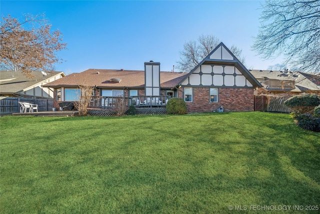 rear view of property with a deck, fence, a yard, brick siding, and a chimney