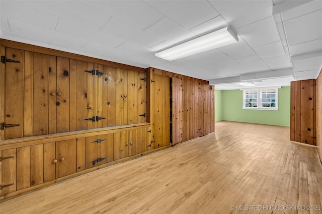 basement with light hardwood / wood-style flooring and wood walls