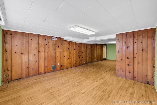 basement with light hardwood / wood-style flooring and wooden walls