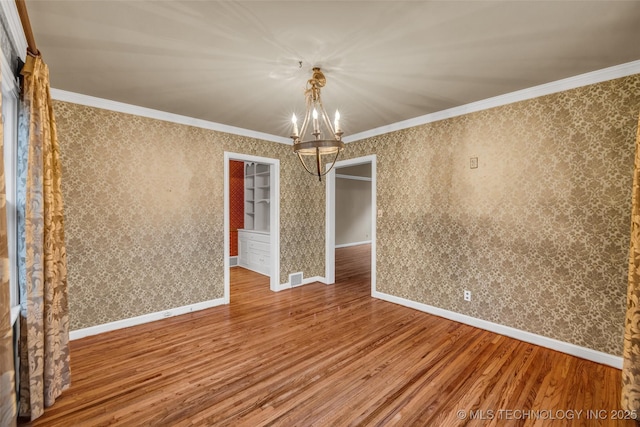 spare room with wood-type flooring, crown molding, and a chandelier