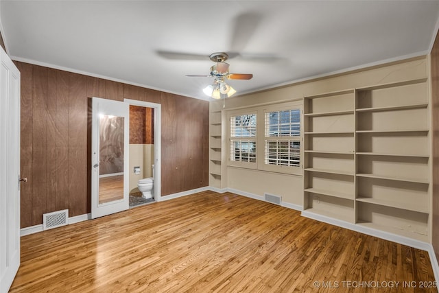 unfurnished bedroom featuring hardwood / wood-style floors, wood walls, ceiling fan, connected bathroom, and ornamental molding